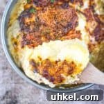 A wooden spoon lifting up a serving of air fryer scalloped potatoes out of a cake pan.