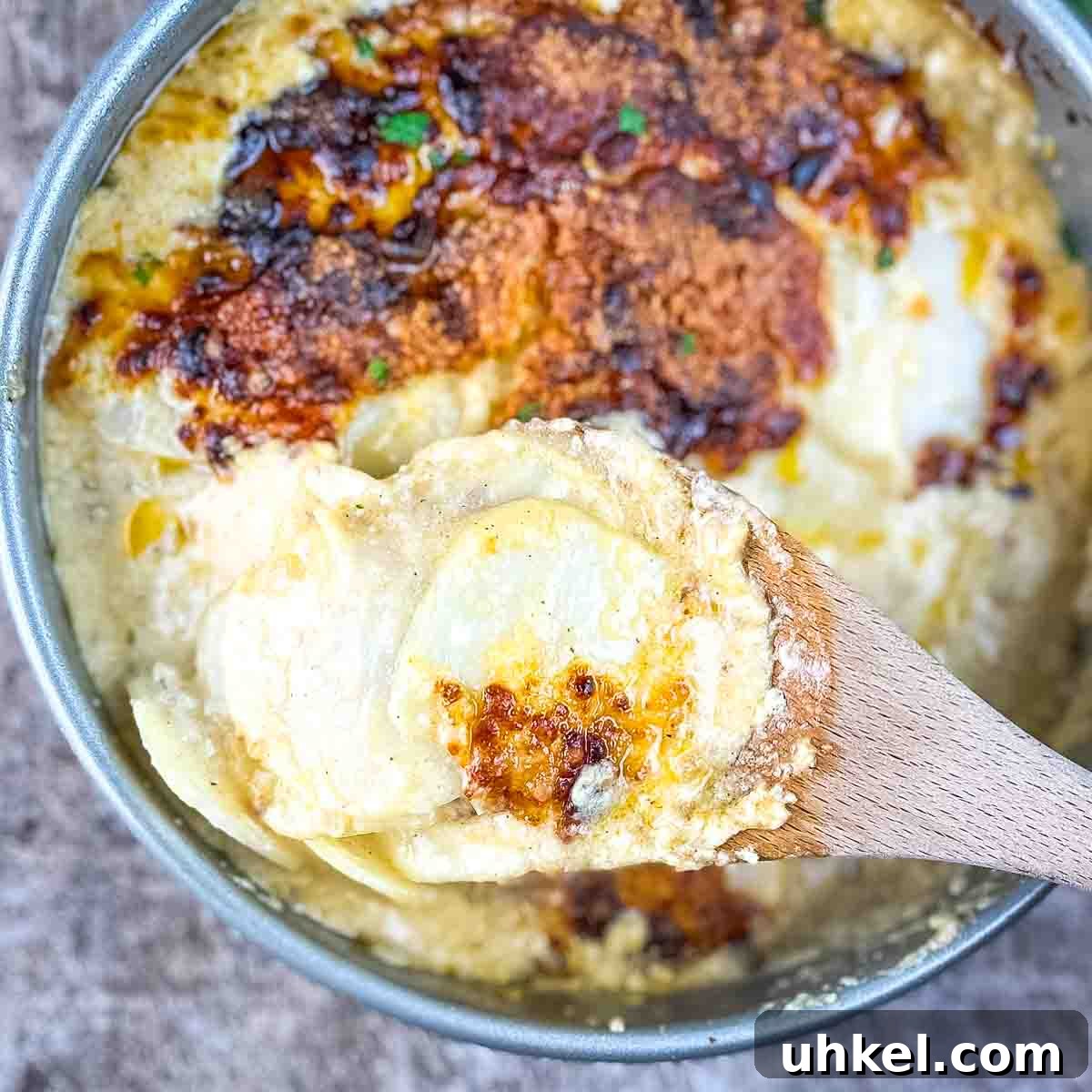 Crispy Cheesy Scalloped Potatoes Made in the Air Fryer 5 A wooden spoon lifting a serving of golden, tender scalloped potatoes, showcasing the creamy sauce and melted cheese topping.