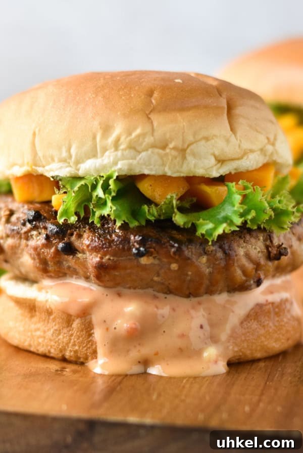 Juicy Mexican-Style Grilled Chicken with Zesty Marinade 14 Chicken teriyaki burgers on a wood serving dish topped with lettuce and chopped mangoes.
