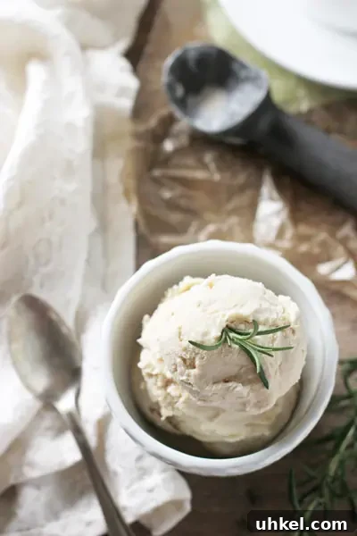 Recipe for dreamy, creamy rosemary ice cream! A sweet vanilla ice cream base infused with just the right amount of fresh rosemary! A white bowl of Rosemary Ice Cream with a scooper to the side.