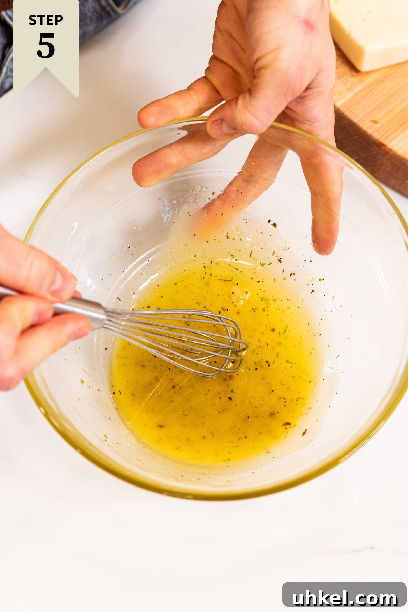 Slow-Cooked Italian Roast Pork Sandwich Recipe 13 Hand stirring together a yellow-colored Italian dressing in a glass bowl with whisk on white countertop.