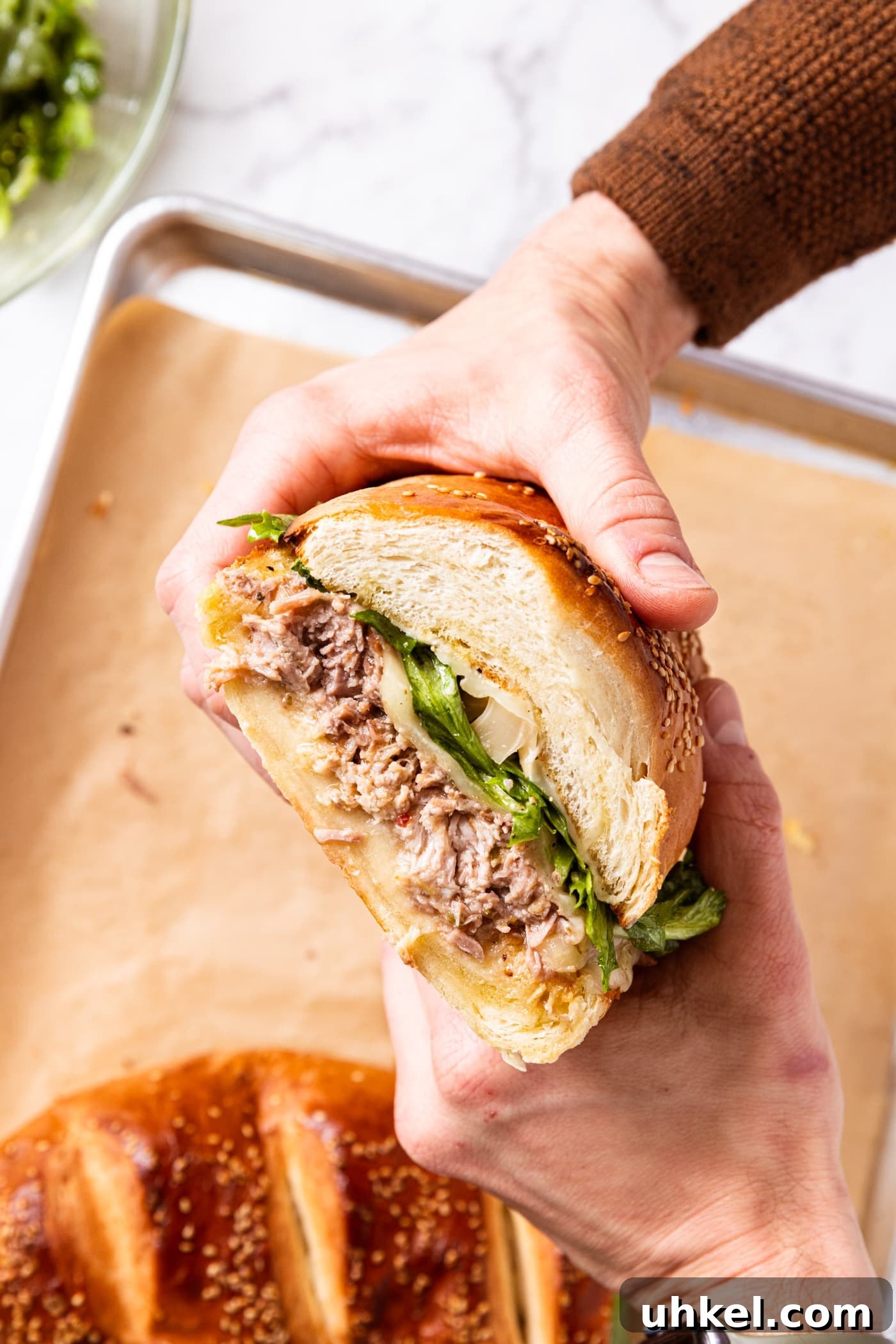 Slow-Cooked Italian Roast Pork Sandwich Recipe 17 Two hands holding half of roasted pork sandwich showing interior filled with pulled pork, greens, and cheese with the texture of the bread.