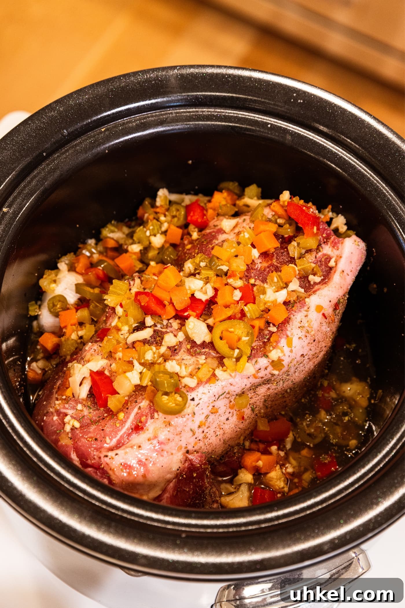 Slow-Cooked Italian Roast Pork Sandwich Recipe 8 Slow cooker sitting on countertop with raw piece of pork shoulder with mixed pickled vegetable mixture all over the top with brown liquid in bottom of container.