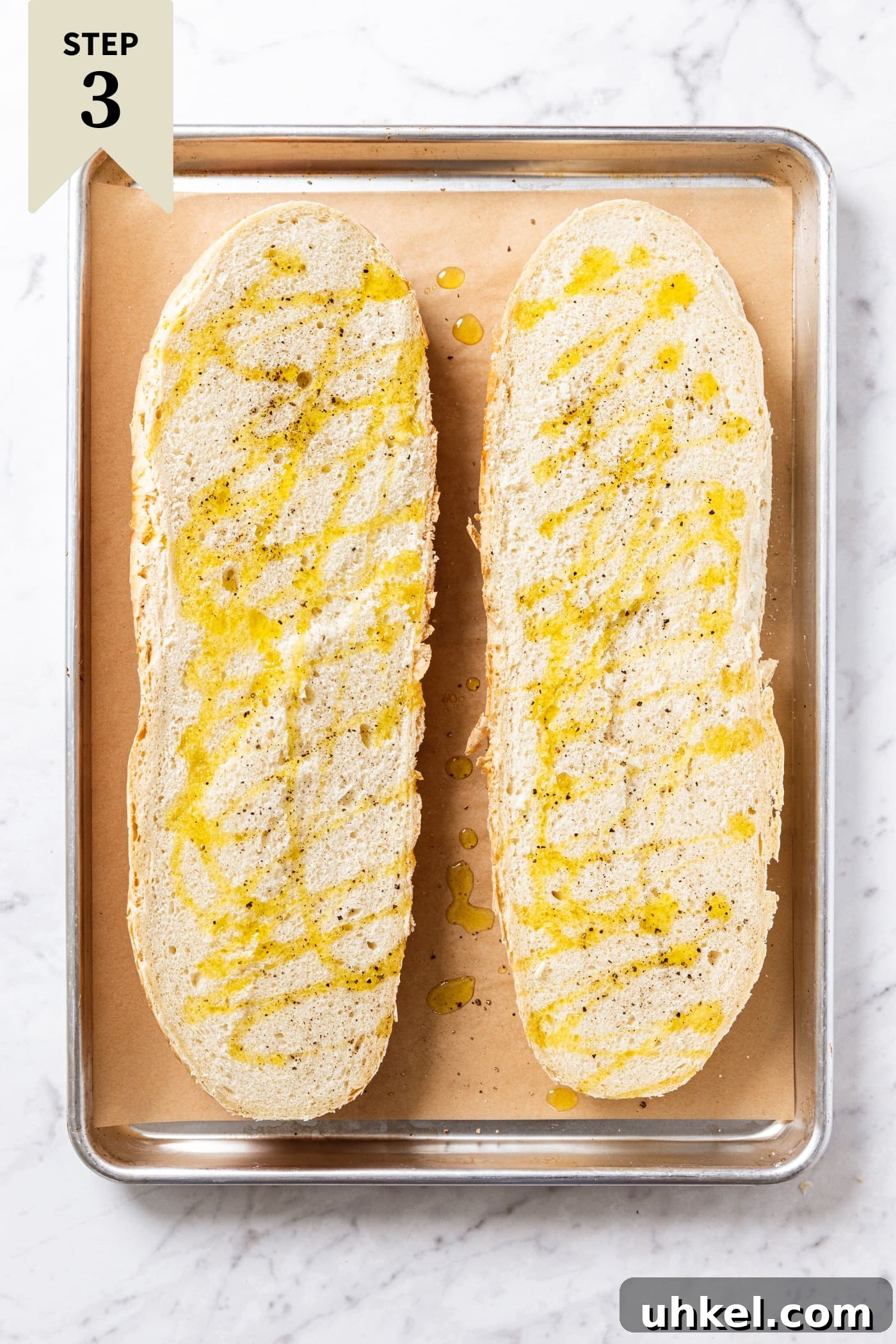 Slow-Cooked Italian Roast Pork Sandwich Recipe 9 White marble surface with parchment-lined sheet pan with untoasted bread drizzled with olive oil and sprinkled with salt and black pepper right before going into the oven.