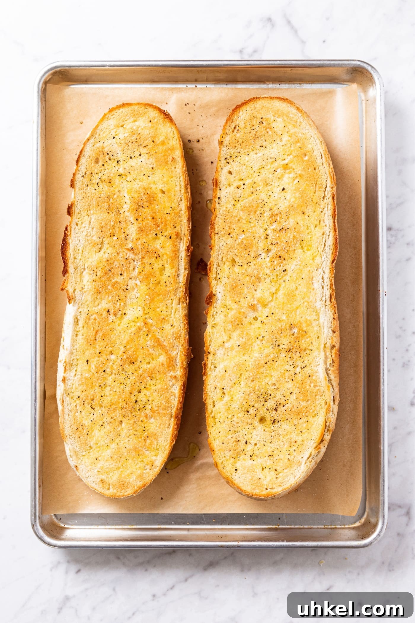 Slow-Cooked Italian Roast Pork Sandwich Recipe 10 White marble surface with parchment-lined baking sheet with toasted loaves of French bread after coming out of the oven golden brown.