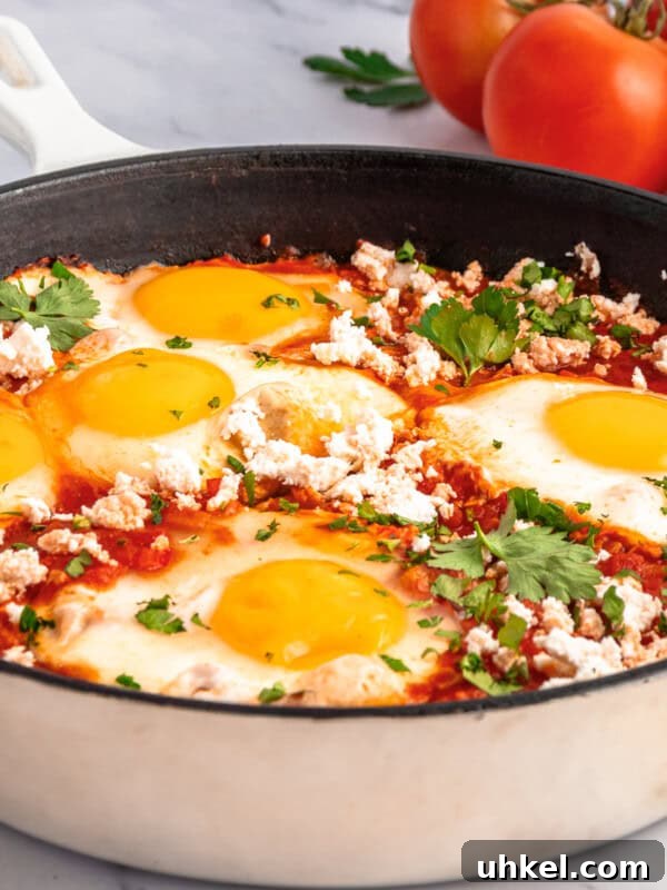 A skillet filled with a classic Shakshouka, featuring poached eggs in tomato sauce topped with crumbled cheese.