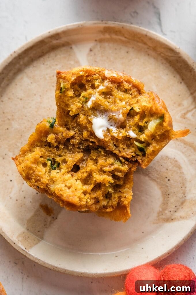 Moist Pumpkin Zucchini Muffins with Warm Spices 3 Close up of a pumpkin zucchini muffin pulled apart in half to show the tender interior, with a pat of butter partially melted on one open half.