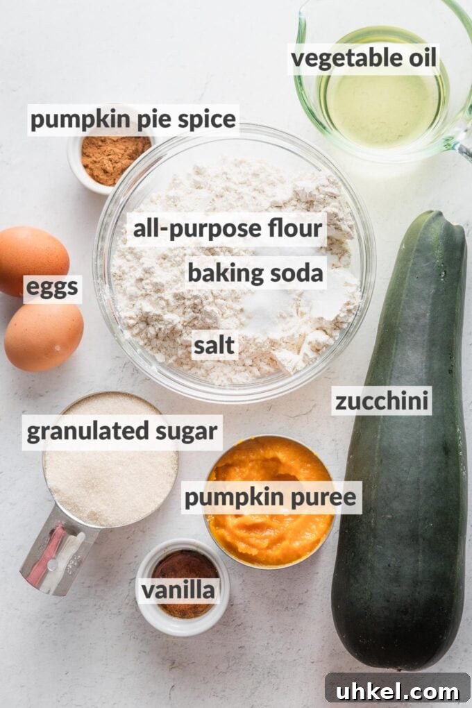 Moist Pumpkin Zucchini Muffins with Warm Spices 4 Labeled overhead photo of all-purpose flour, baking soda, salt, a whole zucchini, an open can of pumpkin puree, vanilla extract, vegetable oil, granulated sugar, two eggs, and pumpkin pie spice, in prep bowls and ready to bake.