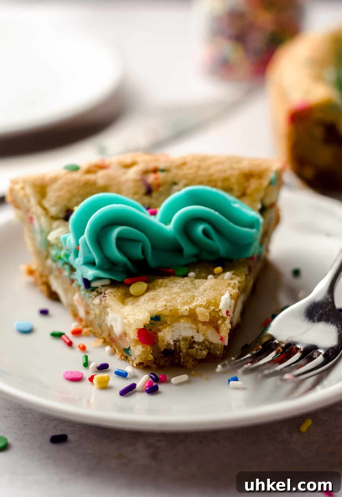 a slice of funfetti sugar cookie cake on a plate with a bite taken out of it