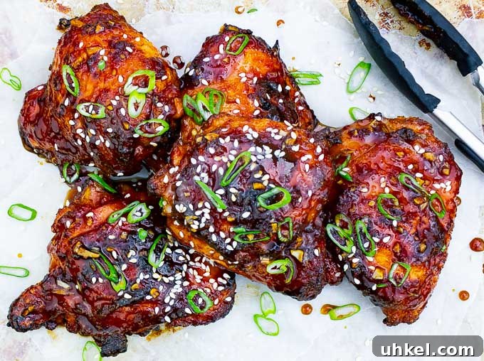 Sticky Asian-Style Grilled Chicken Thighs with Sweet Glaze 7 five pieces of Sticky Asian Grilled Chicken Thighs on white background with tongs