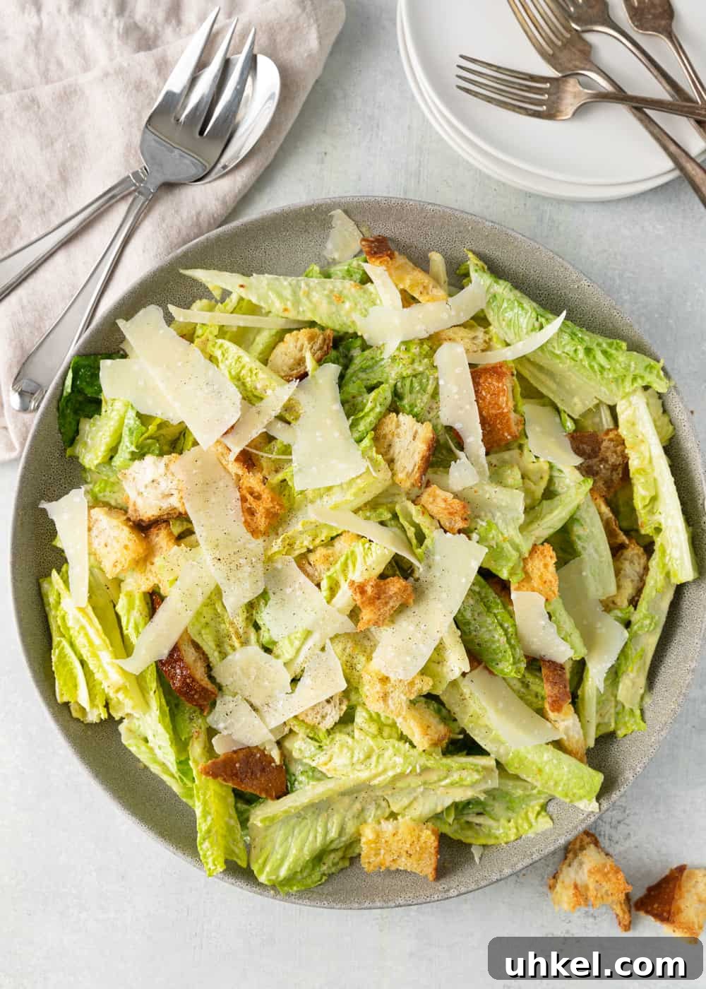 Authentic Caesar Salad Recipe with Creamy Homemade Dressing 5 bowl of Caesar salad surrounded by plates, napkins, and silverware