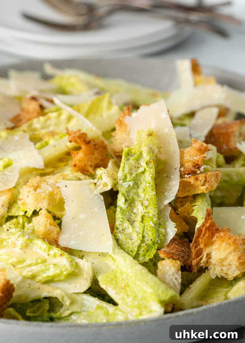 Authentic Caesar Salad Recipe with Creamy Homemade Dressing 6 close up of salad with croutons and cheese with plates and fork in the background