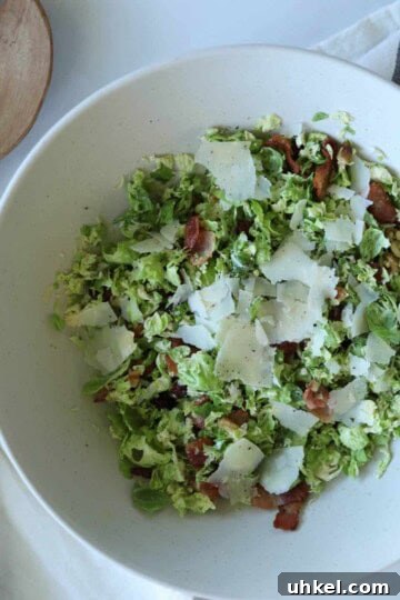 Shaved brussel sprout salad in salad bowl topped with parmesan cheese.