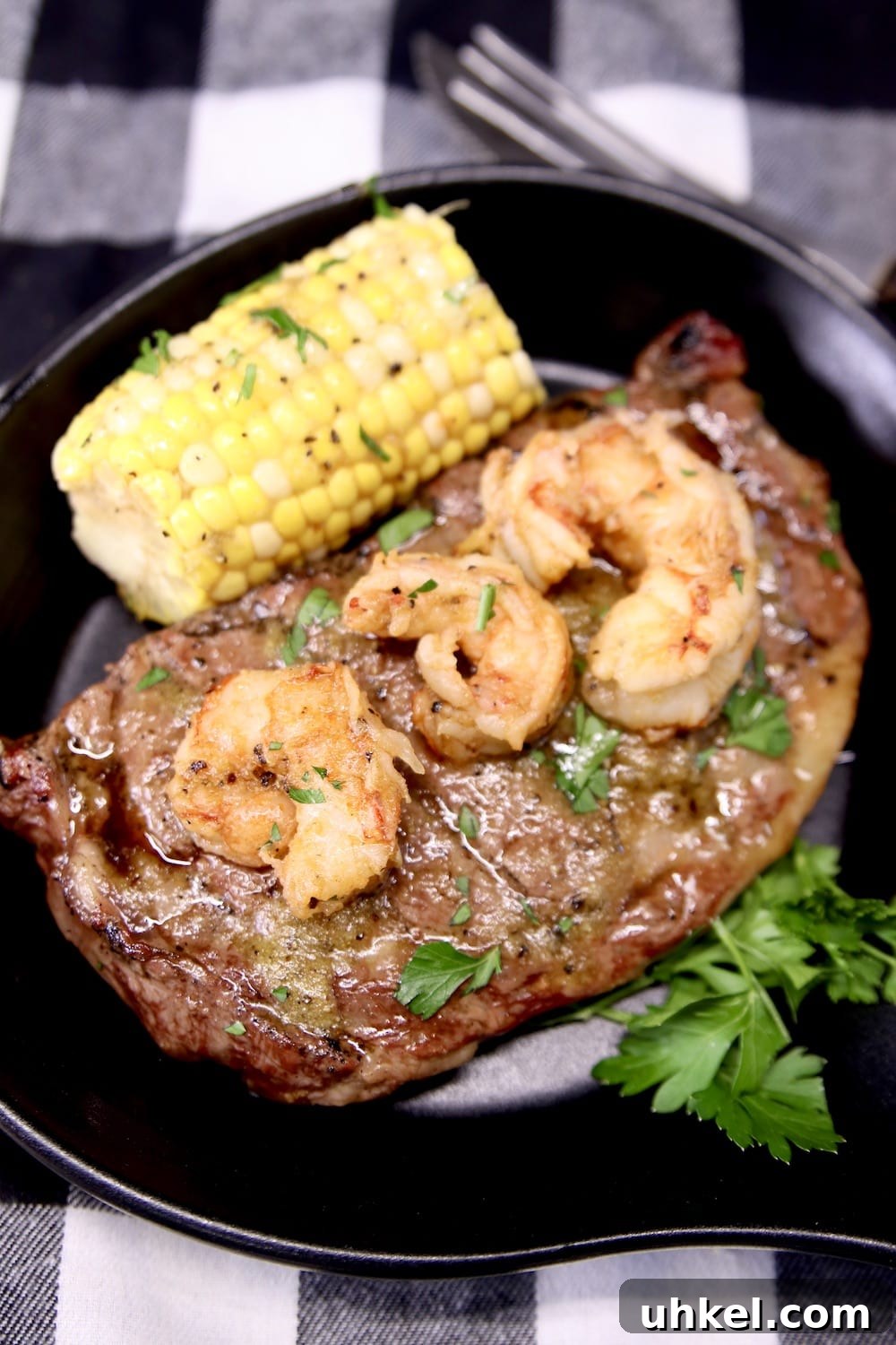 Chile Butter Ribeyes with Shrimp black serving skillet with ribeye steak topped with shrimp. Served with corn on the cob