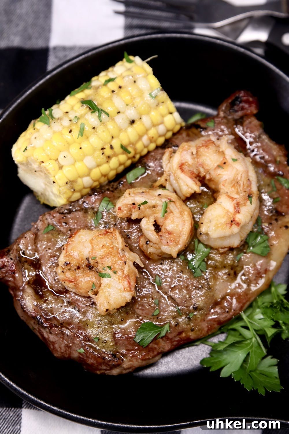 Grilled Chile Butter Ribeyes with Shrimp serving skillet with grilled steak, 3 shrimp, corn on the cob