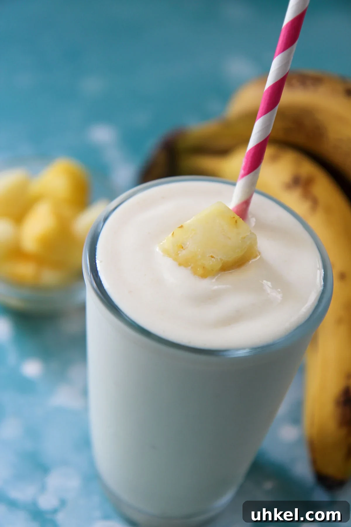 Creamy Pineapple Banana Smoothie Recipe for Tropical Energy 2 pineapple banana smoothie in a glass with a pink a white straw and fruit on top