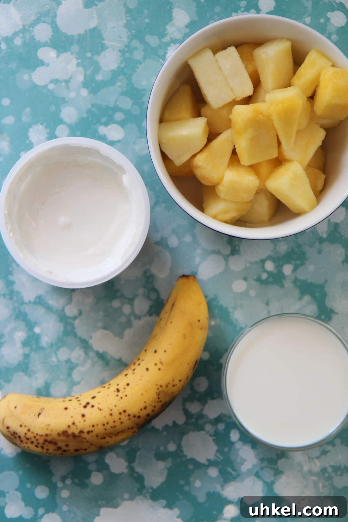 Creamy Pineapple Banana Smoothie Recipe for Tropical Energy 3 frozen pineapples, milk, yogurt, and banana on a blue and white board.