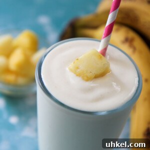 Creamy Pineapple Banana Smoothie Recipe for Tropical Energy 5 pineapple banana smoothie in a glass with a pink a white straw and fruit on top