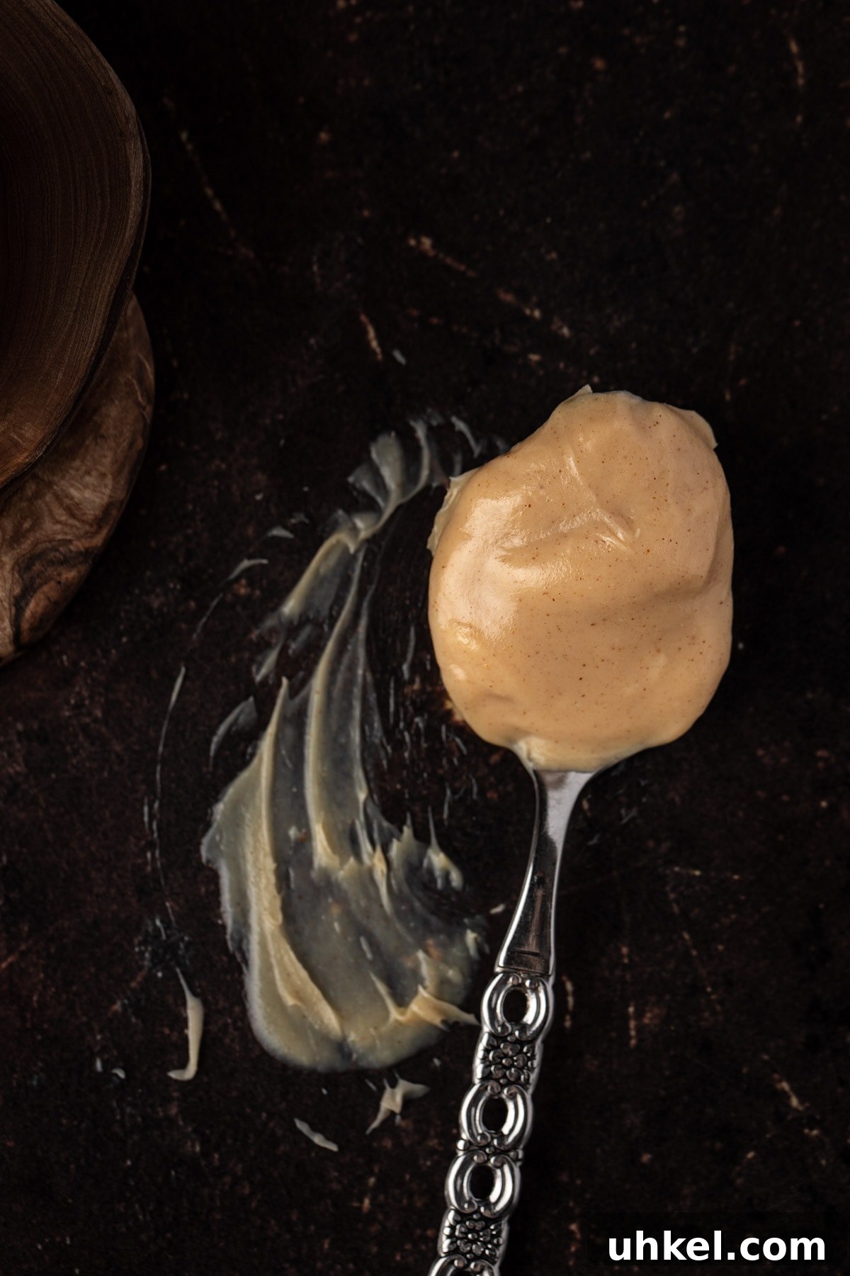 Decadent Peanut Butter Ganache Recipe for Cakes and Desserts 3 Overhead view of a spoonful of peanut ganache on a dark brown table.