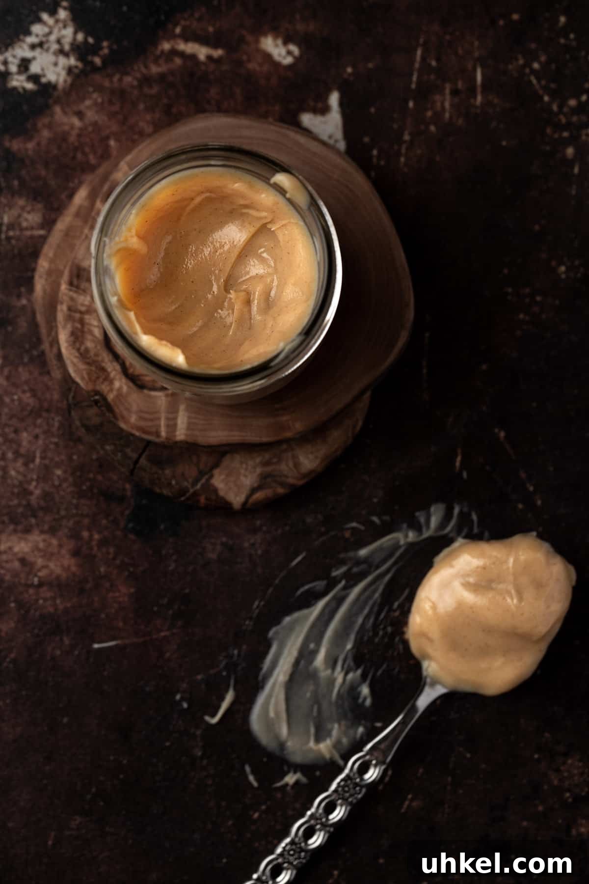 Decadent Peanut Butter Ganache Recipe for Cakes and Desserts 7 Overhead view of a mason jar of ganache, on a dark brown table, next to a metal spoonful of ganache.