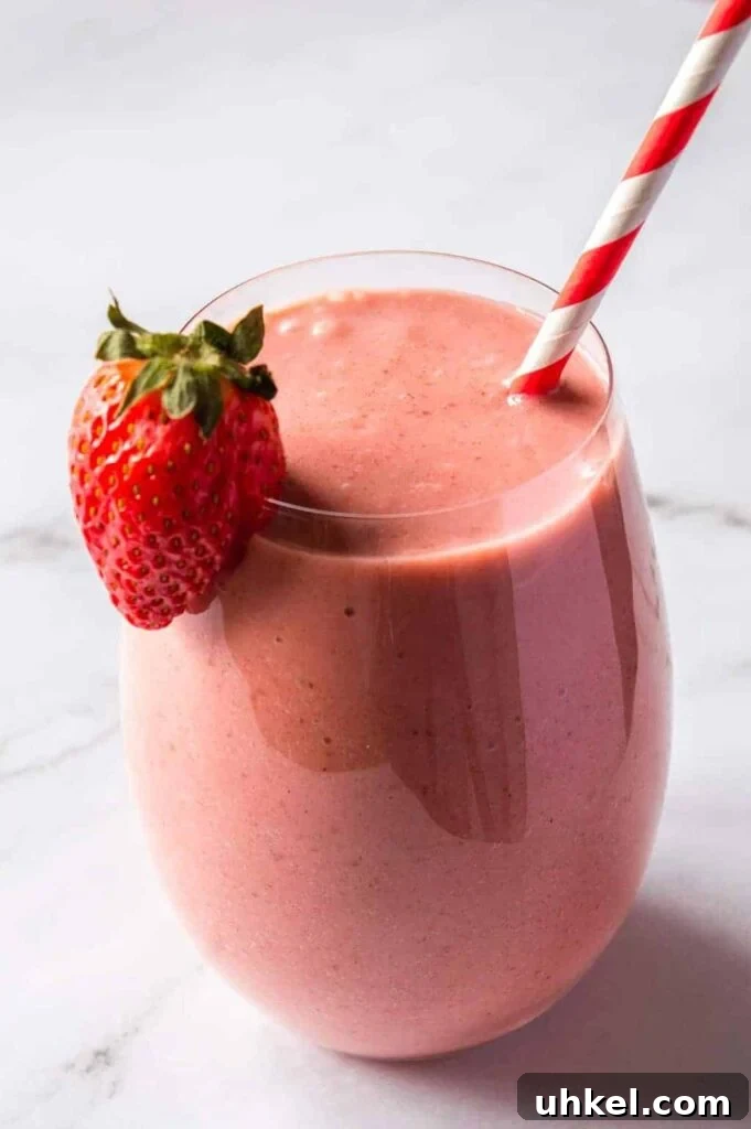 Creamy Strawberry Banana Vegan Smoothie Recipe 2 Front view of a round glass with a pink smoothie, a strawberry on the rim, and a red and white paper straw
