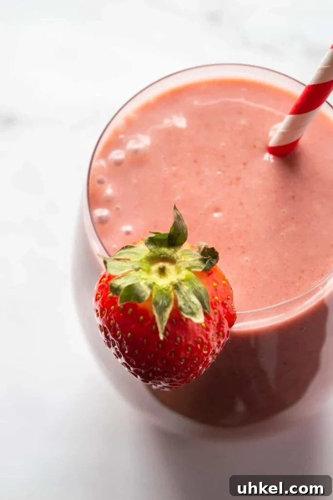 Creamy Strawberry Banana Vegan Smoothie Recipe 4 Top-down view of a glass filled with pink smoothie with a strawberry on the edge and a striped straw