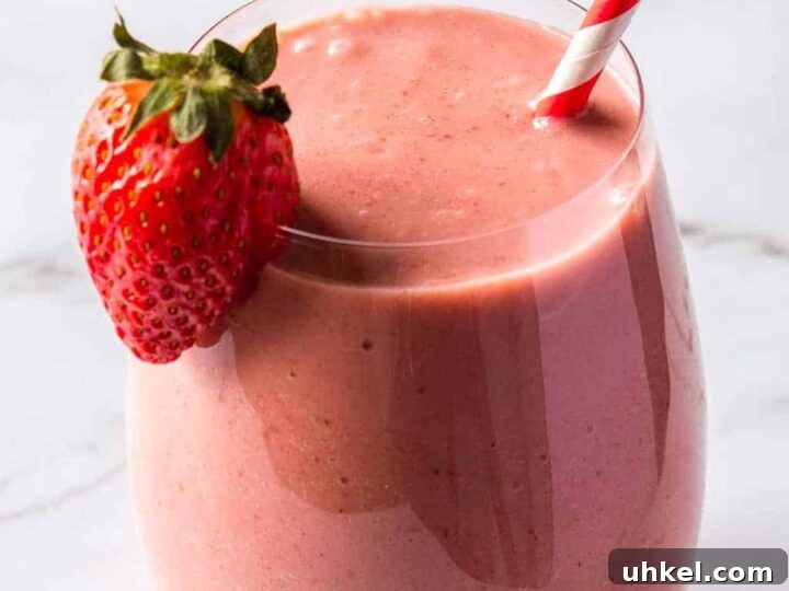 Front view of a round glass with a pink smoothie, a strawberry on the rim, and a red and white paper straw