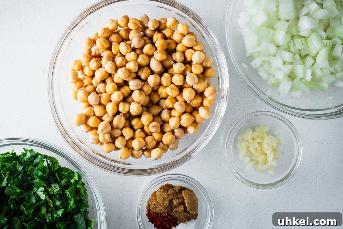 Crispy Authentic Middle Eastern Falafel Recipe 3 Falafel ingredients arranged in glass prep bowls, including dried chickpeas that were soaked overnight, chopped onion, garlic, fresh herbs and spices.