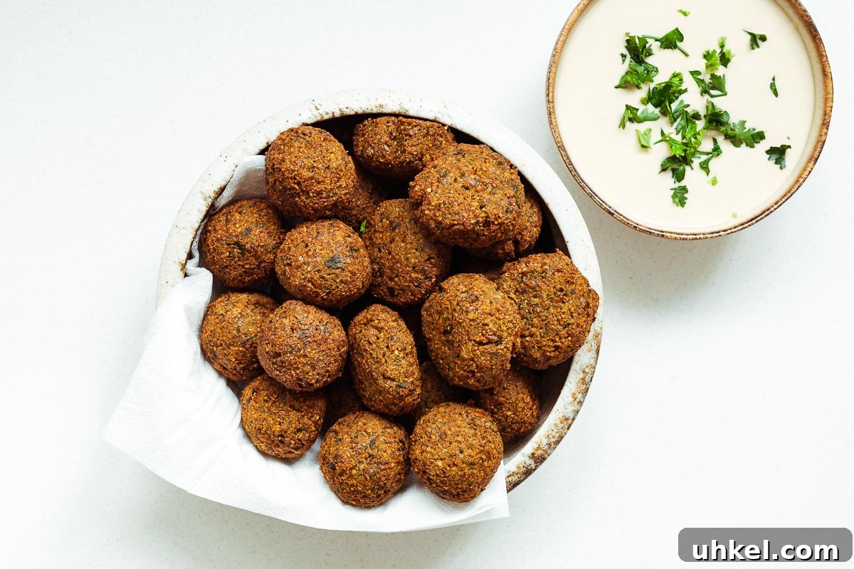 Crispy Authentic Middle Eastern Falafel Recipe 5 A ceramic bowl with crispy falafel balls and falafel patties next to a small bowl of falafel tahini sauce viewed from above.