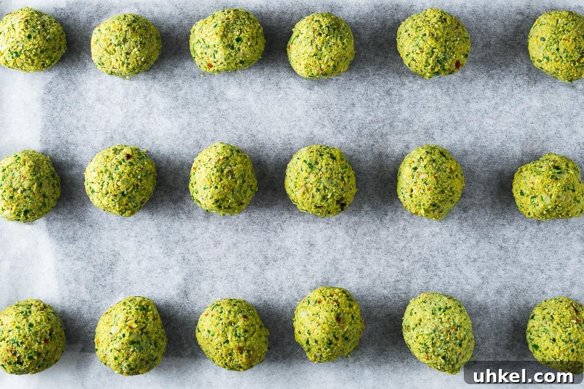 Crispy Authentic Middle Eastern Falafel Recipe 9 Uncooked falafel balls arranged on a parchment-lined baking sheet viewed from above.