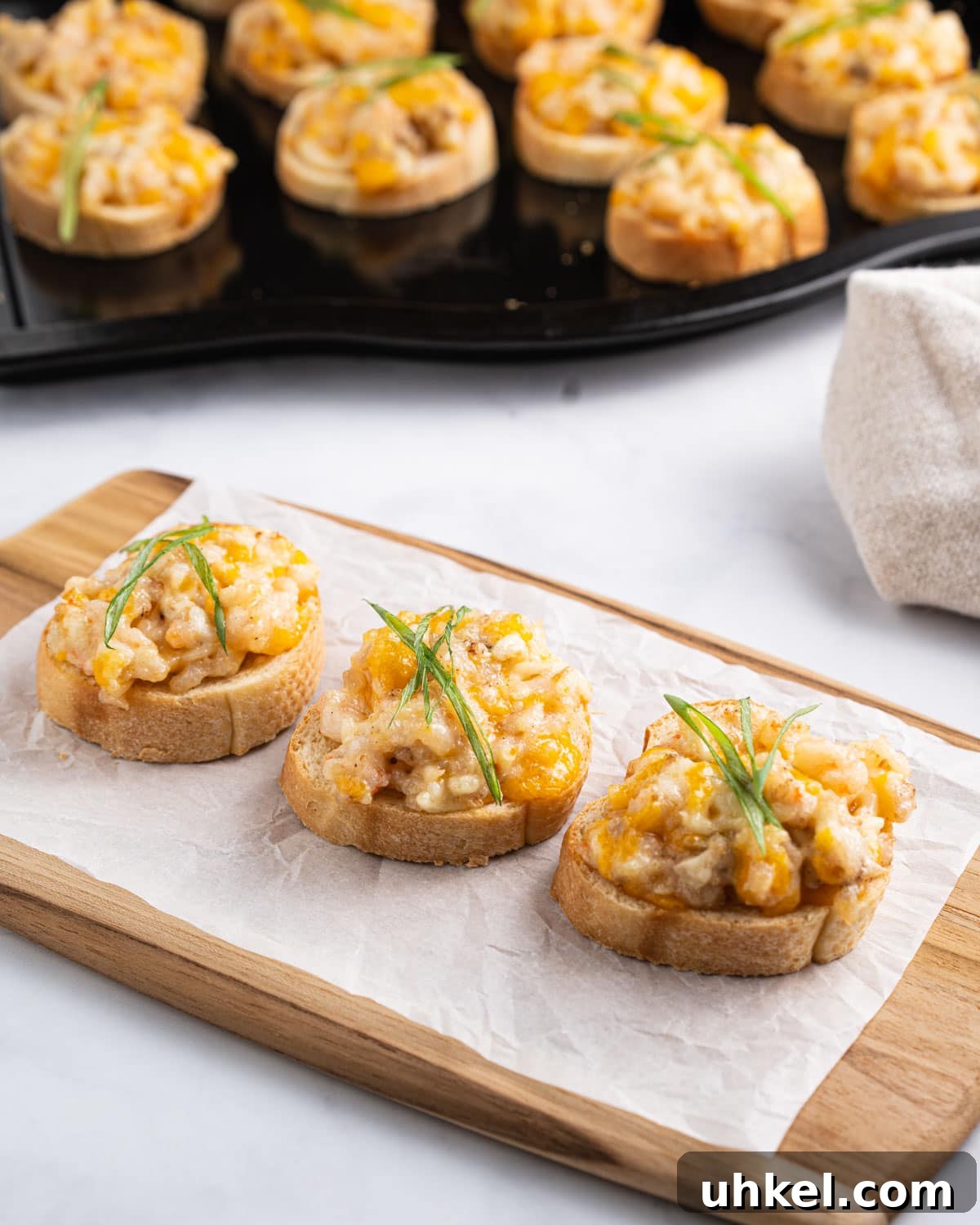 Tray of Vietnamese shrimp toasts in the background and 3 shrimp toasts on a serving board.