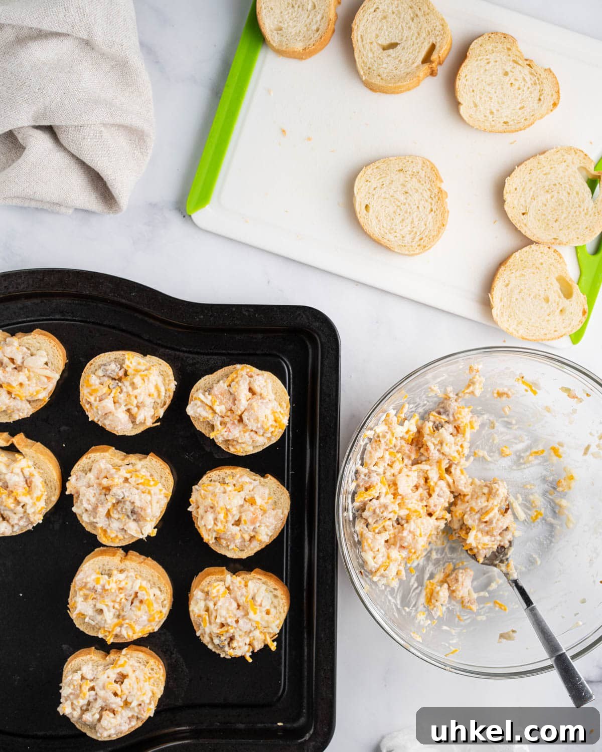 Process of assembling shrimp toast. Cutting board with baguette slices, bowl of shrimp mixture and black baking tray with assembled shrimp toasts.