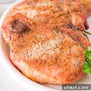 Smoked Pork Chops Recipe: Tender, Juicy Flavor from the Smoker 14 Close-up of juicy smoked pork chops with a crispy rub, served on a white plate with parsley garnish