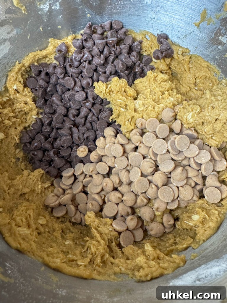 Gooey Chocolate Peanut Butter Oatmeal Bars Recipe 8 Semi sweet chocolate chips and peanut butter chips poured on top of an oatmeal and peanut butter cookie dough in a silver mixing bowl.