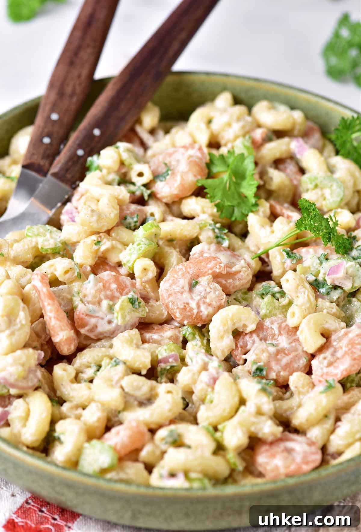 Lemon Garlic Shrimp Pasta Salad with Fresh Herbs 7 Shrimp pasta salad on a green plate with parsley leaves. Wooden serving spoons.