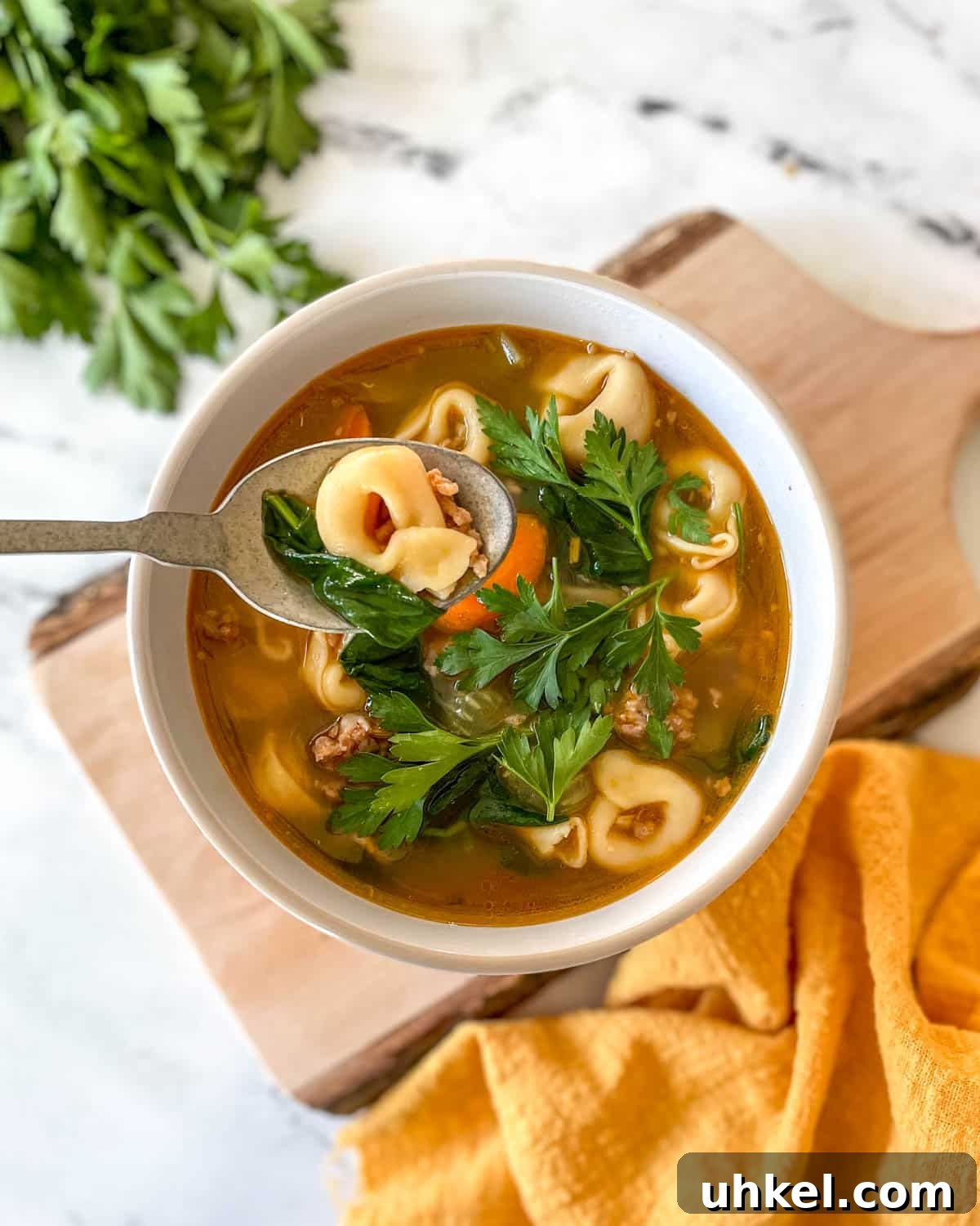 Instant Pot Tortellini Soup Recipe: Creamy Italian Comfort in 20 Minutes 2 A bowl of tortellini soup sits on a rustic wooden cutting board with a yellow linen and a bunch of parsley.