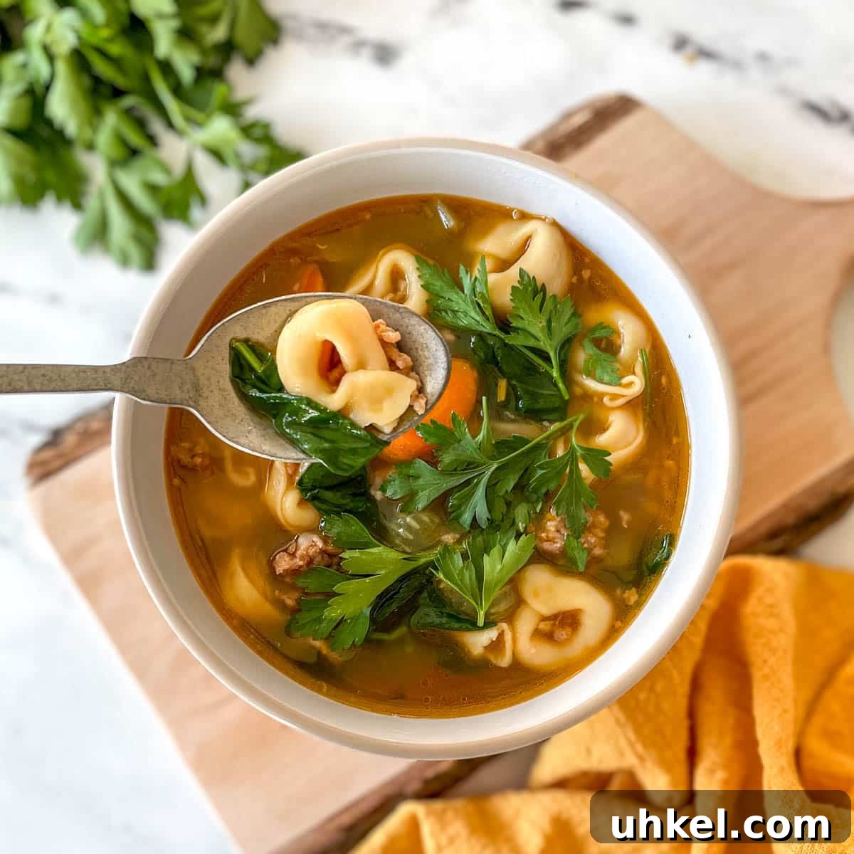 Instant Pot Tortellini Soup Recipe: Creamy Italian Comfort in 20 Minutes 10 A bowl of tortellini soup sits on a rustic wooden cutting board with a yellow linen and a bunch of parsley.