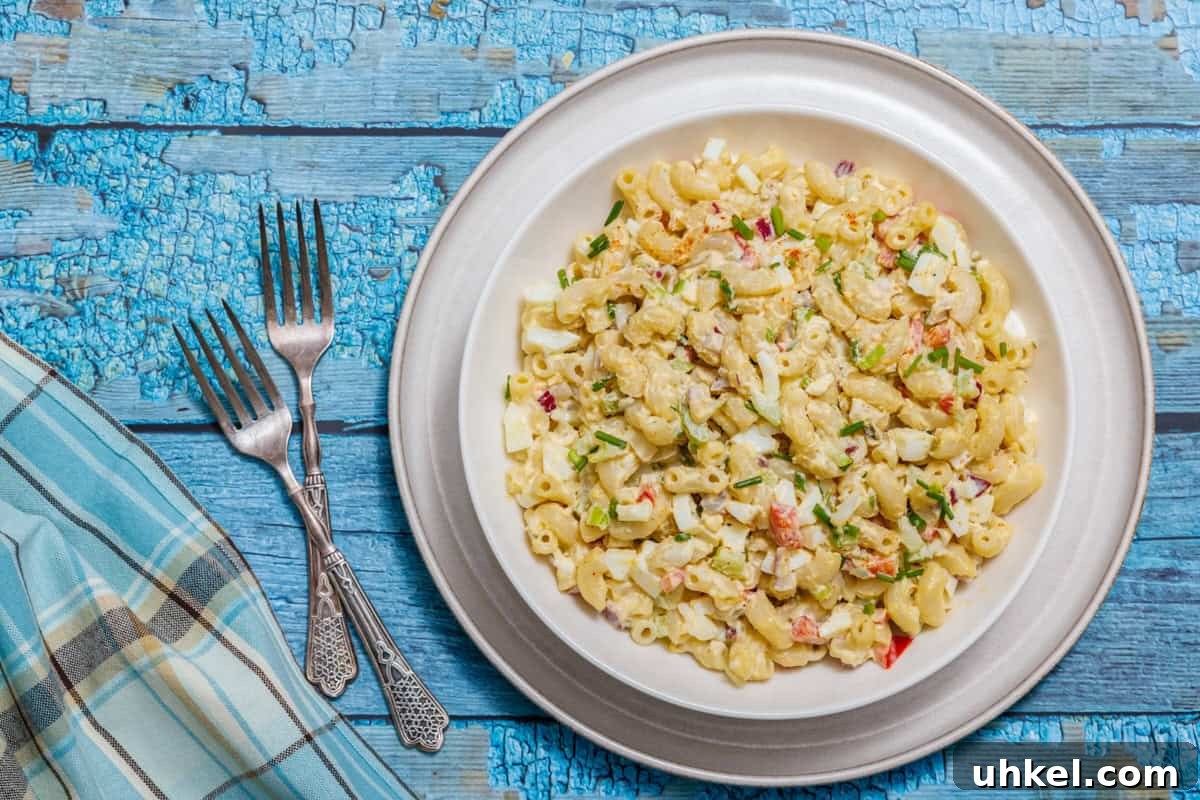 19 Budget-Friendly Dinners That Cut Your Grocery Bill (Delicious!) 3 Plate of Deviled Egg Pasta Salad on a wooden table, accompanied by three forks and a blue plaid napkin.