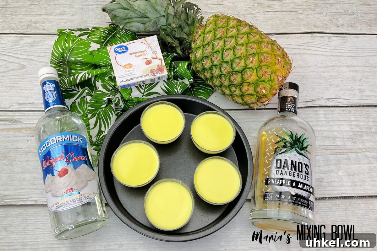 five shots of dole whip in a cake pan, surrounded by bottles of alcohol, gelatin, and pineapple