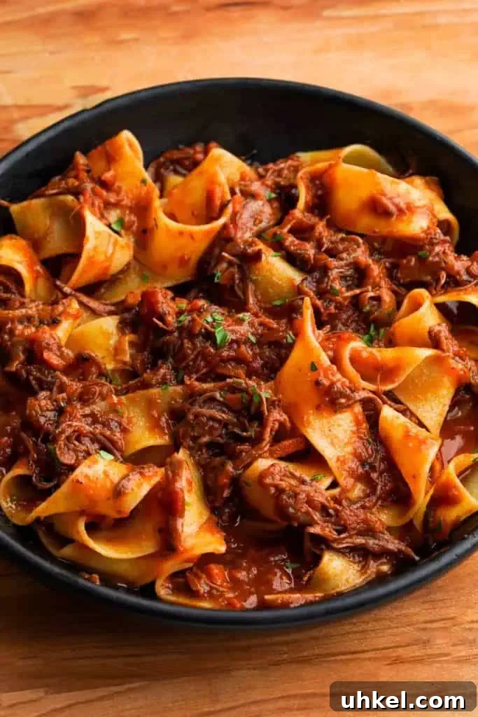 whisper of yum short rib ragu A close-up of short rib ragu served over wide pappardelle pasta in a dark bowl, garnished with fresh parsley.