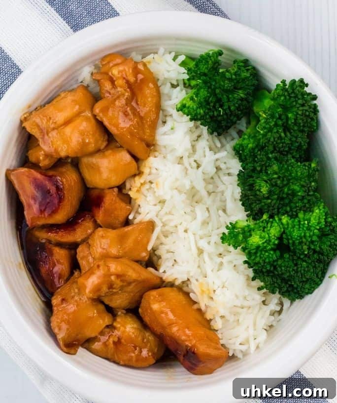 white bowl of teriyaki chicken, rice, and broccoli on a blue and white striped cloth