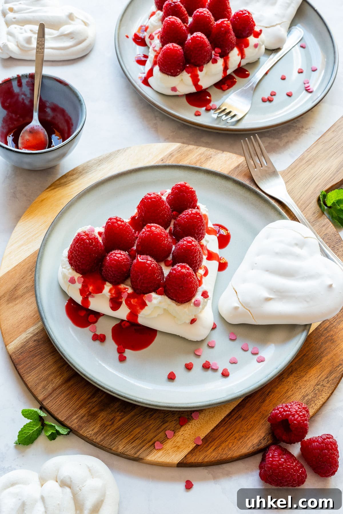Heart-Shaped Mini Pavlovas: Valentine Dessert Recipe Ideas 2 Heart-shaped mini pavlovas with whipped cream, fresh raspberries and raspberry coulis on plates.