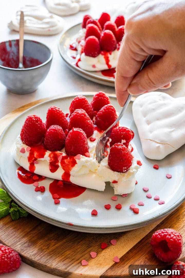 Heart-Shaped Mini Pavlovas: Valentine Dessert Recipe Ideas 11 Cutting into a pavlova heart topped with whipped cream, raspberries and raspberry coulis.