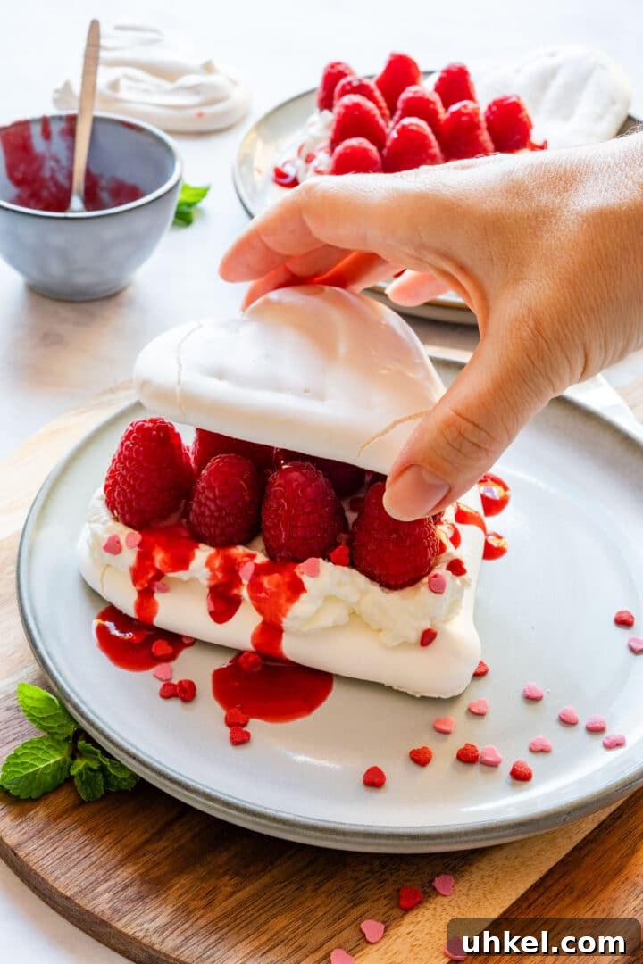 Heart-Shaped Mini Pavlovas: Valentine Dessert Recipe Ideas 10 Stacking two meringue hearts with whipped cream and raspberries in the middle.