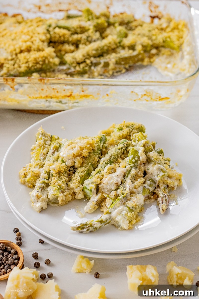 Crispy Baked Parmesan Asparagus Recipe 2 sliced asparagus baked in parmesan cream sauce on a white plate