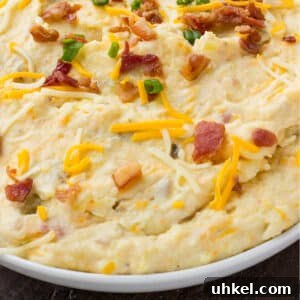 Creamy Instant Pot Mashed Potatoes Recipe 15 A bowl of Instant pot mashed potatoes on the table with some bacon, green onions and shredded cheese sprinkled on top.