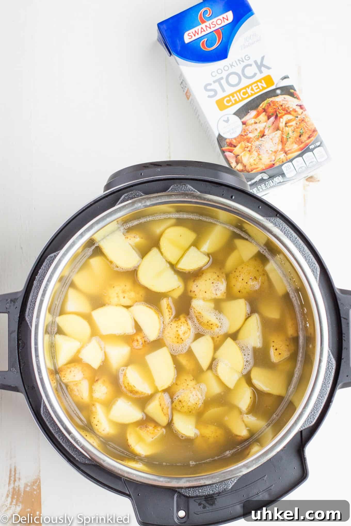 Creamy Instant Pot Mashed Potatoes Recipe 3 Cubes of potatoes in the instant pot with a container of broth to the side.