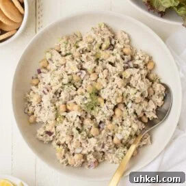 Tuna and Chickpea Salad with Lemon-Dill Dressing 7 A serving bowl of chickpea tuna salad with a serving spoon, nearby lemon wedges, crackers, and greens.