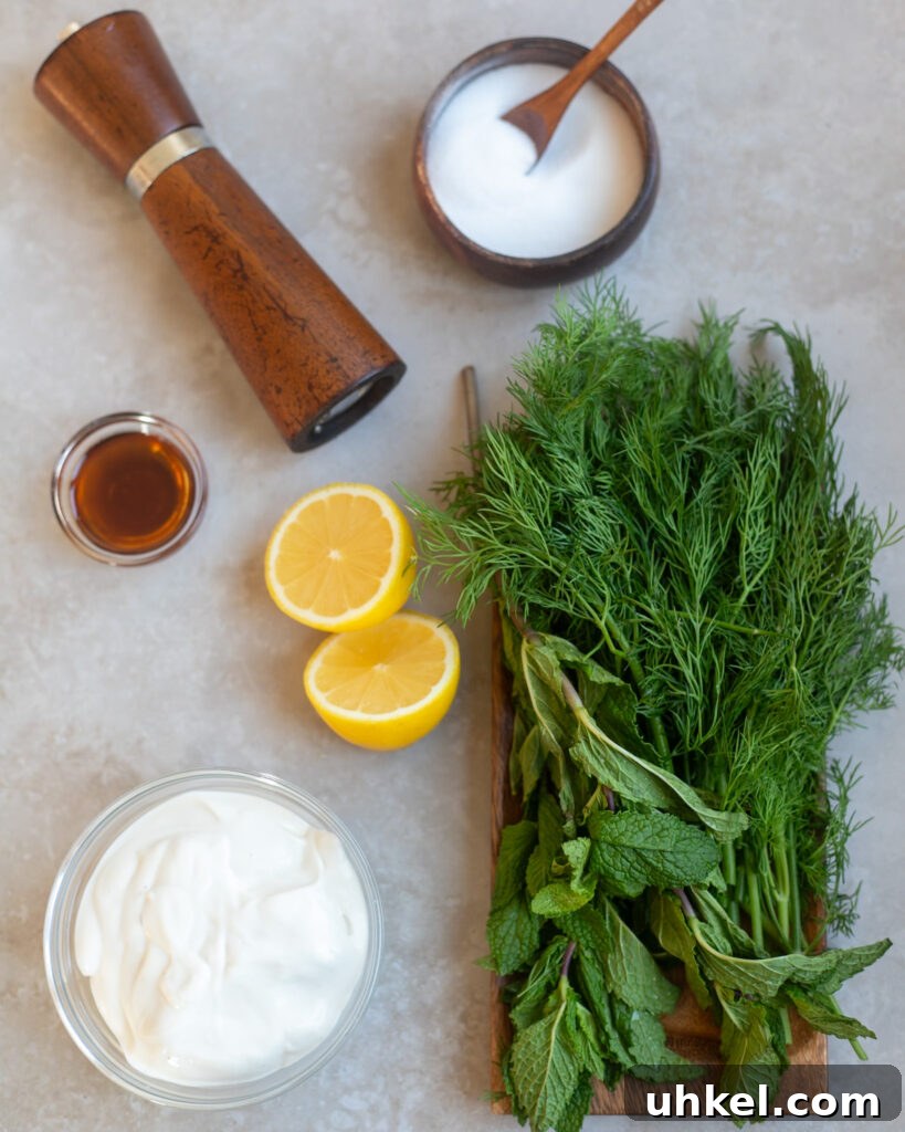 Vegan Creamy Yogurt and Herb Dressing Recipe 3 overhead view of a gray surface on which sit the ingredients to make creamy yogurt herb salad dressing including vegan yogurt, fresh lemons, maple syrup, fresh dill and mint, salt and pepper.