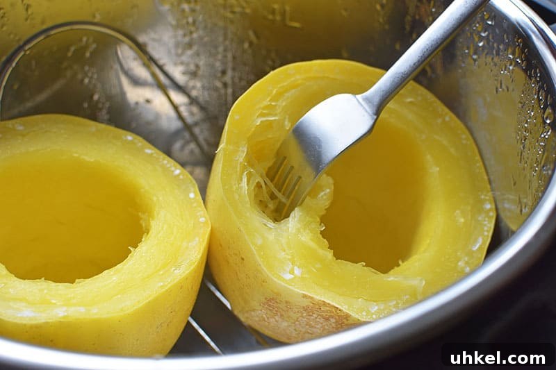 Instant Pot Spaghetti Squash — Quick Foolproof Pressure Cooker Recipe 13 Close up of an open Instant Pot after the spaghetti squash is cooked. There is a fork poking in the spaghetti squash half on the right and the bright yellow squash flesh is shredded like noodles.